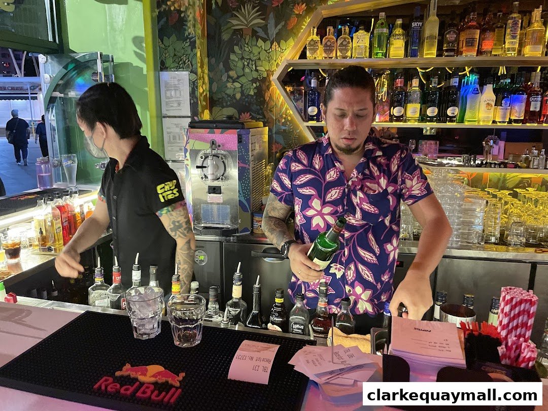 Bartenders preparing drinks behind a bar stocked with bottles and glassware.