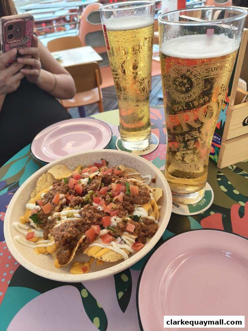 A bowl of loaded nachos and two glasses of beer on a colorful table.