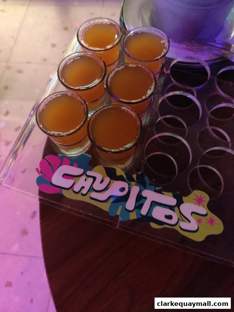 A tray of six orange shots with the shop name 'Chupitos' visible.