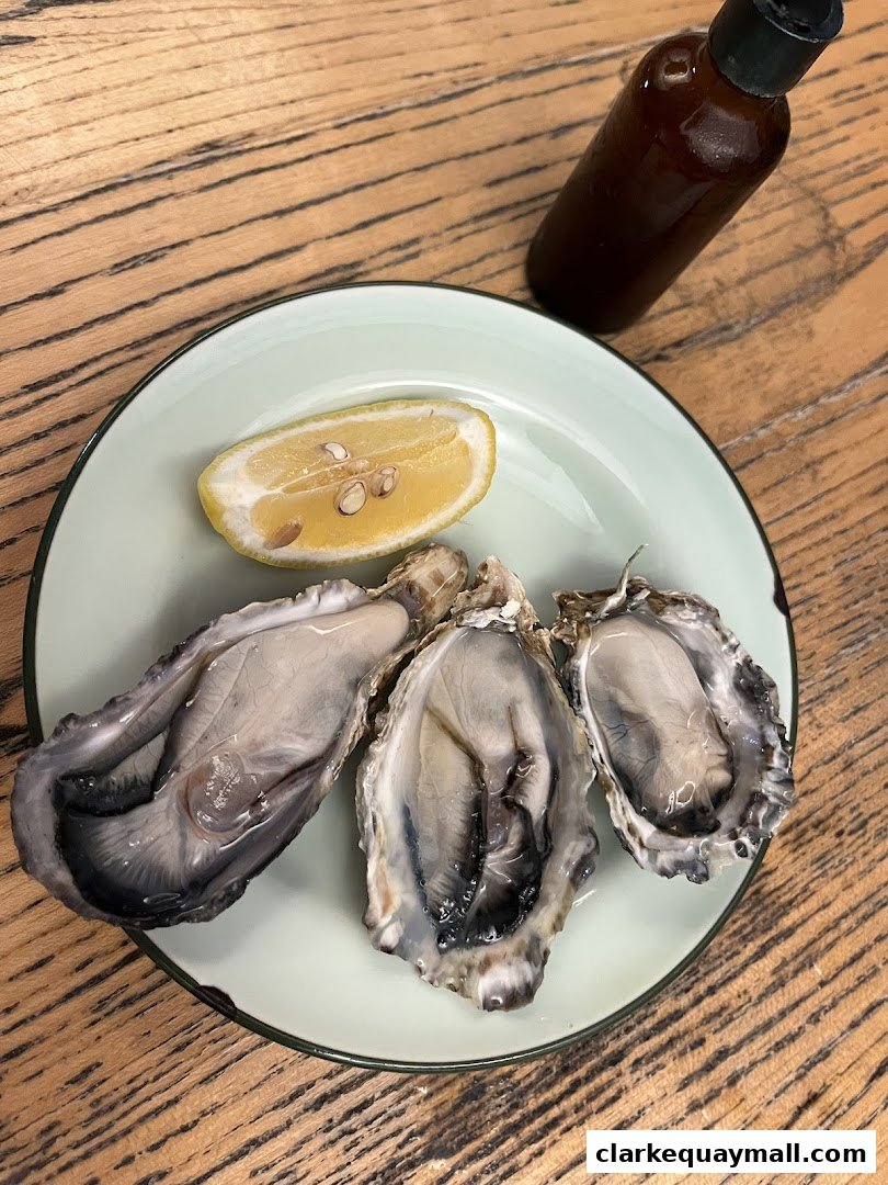 Three fresh oysters served on a plate with a lemon wedge and a bottle of sauce.