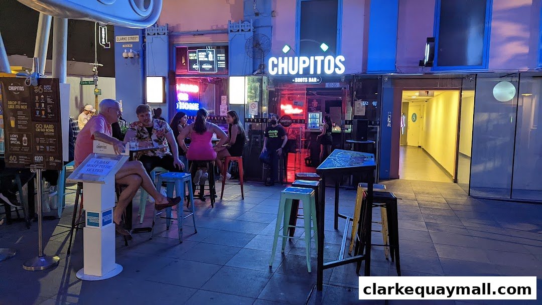 People sit at tables outside a brightly lit bar called Chupitos, a shots bar.