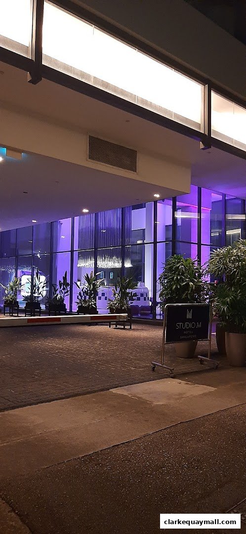 The entrance of Studio M Hotel Singapore at night, illuminated with purple lights.