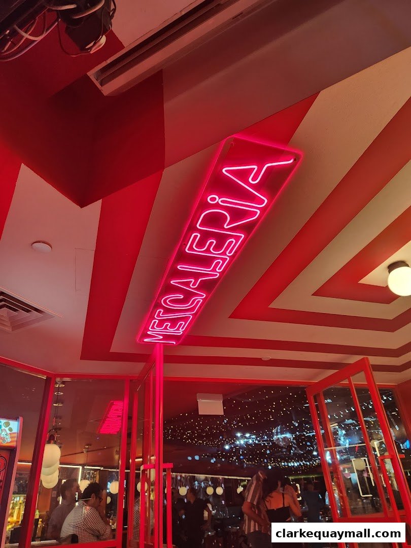 A neon sign spelling 'MECALERIA' hangs above a vibrant interior with red and white striped ceiling.