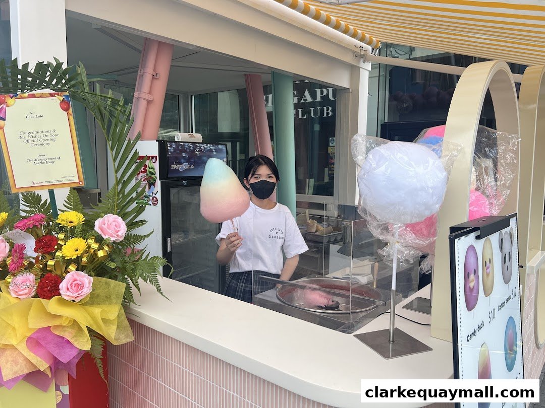 A smiling employee at Cocolato holds a colorful cotton candy stick.