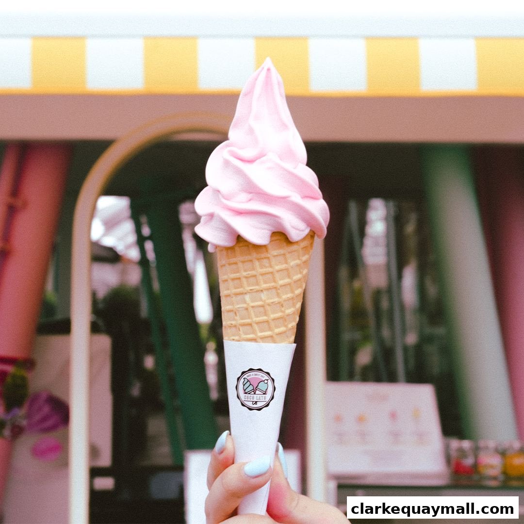 A hand holds a pink soft-serve ice cream cone with the shop's logo.