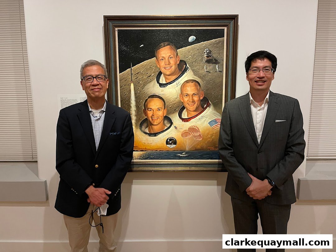 Two men stand in front of a painting depicting the Apollo 11 astronauts.