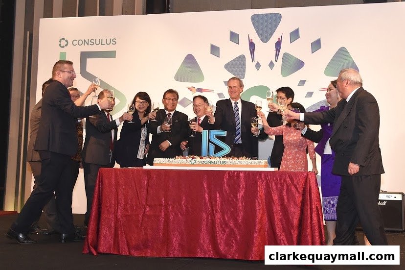 A group of people in formal attire raising glasses in a toast around a cake celebrating 15 years.