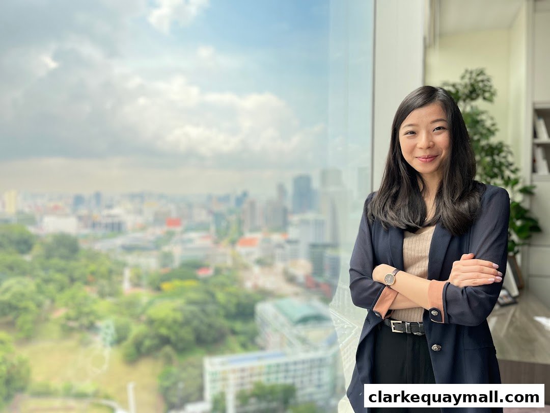 A professional woman stands with her arms crossed in front of a window overlooking a city skyline.