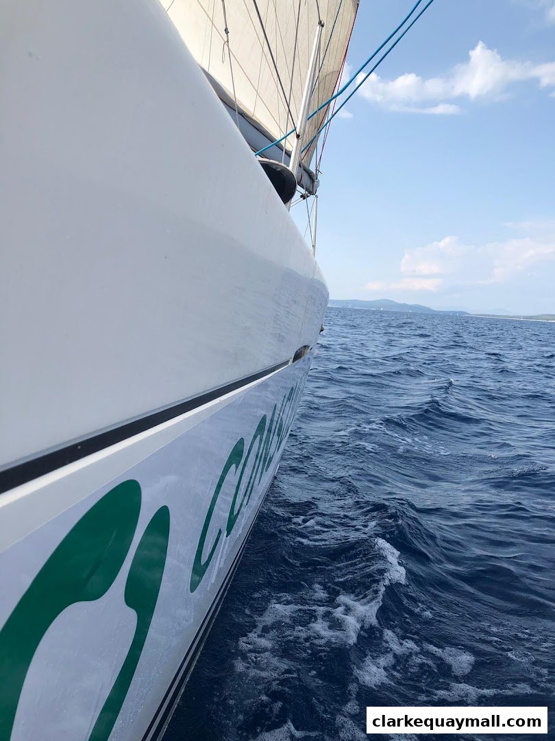 A sailboat glides through blue water under a partly cloudy sky.