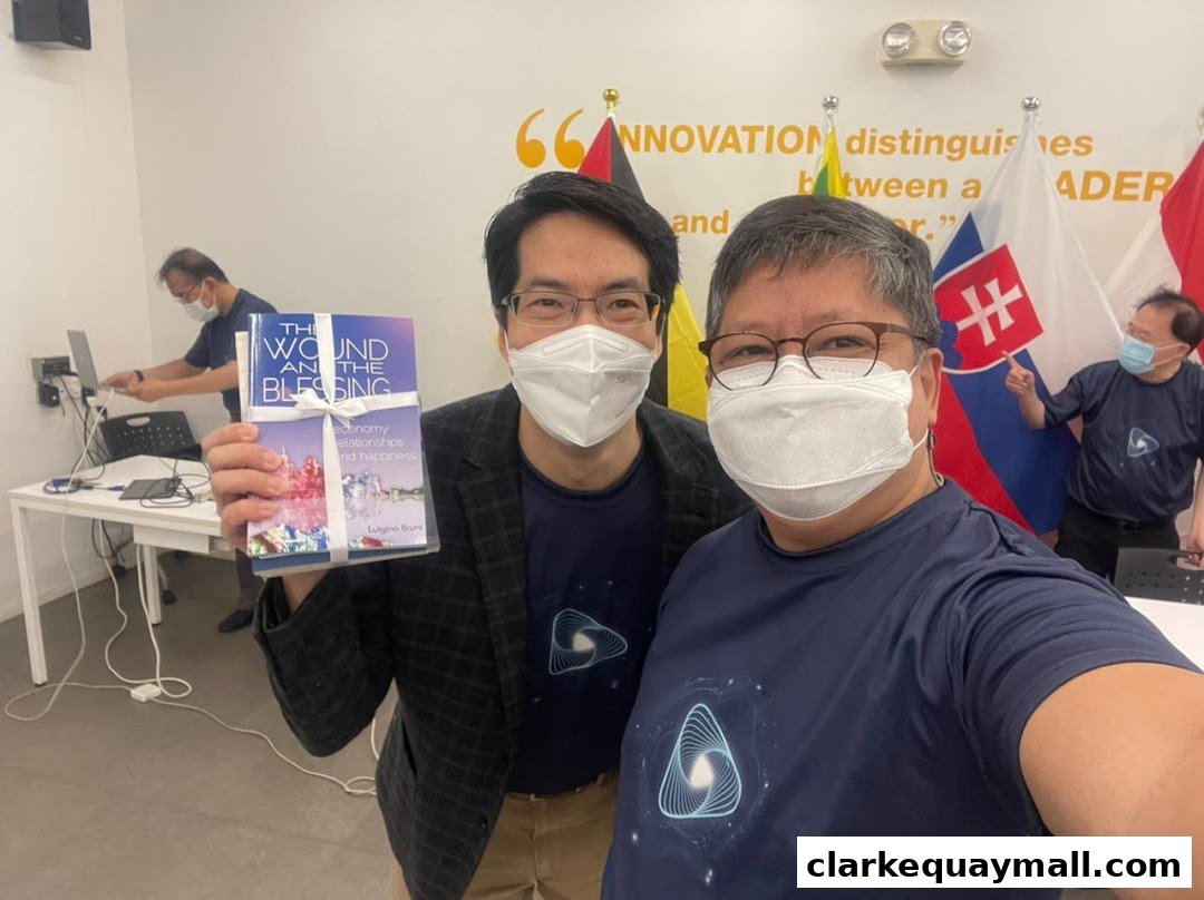 Two men in masks pose for a selfie, one holding a book titled 'The Wound and the Blessing'.