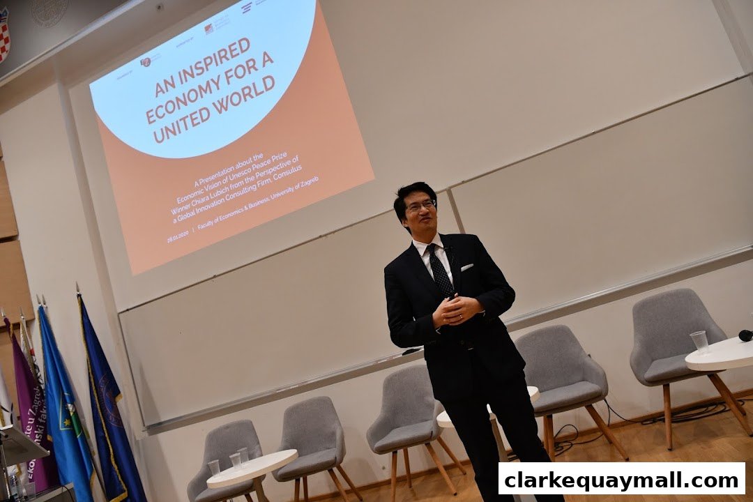 A presenter in a suit stands before a screen displaying 'An Inspired Economy for a United World'.