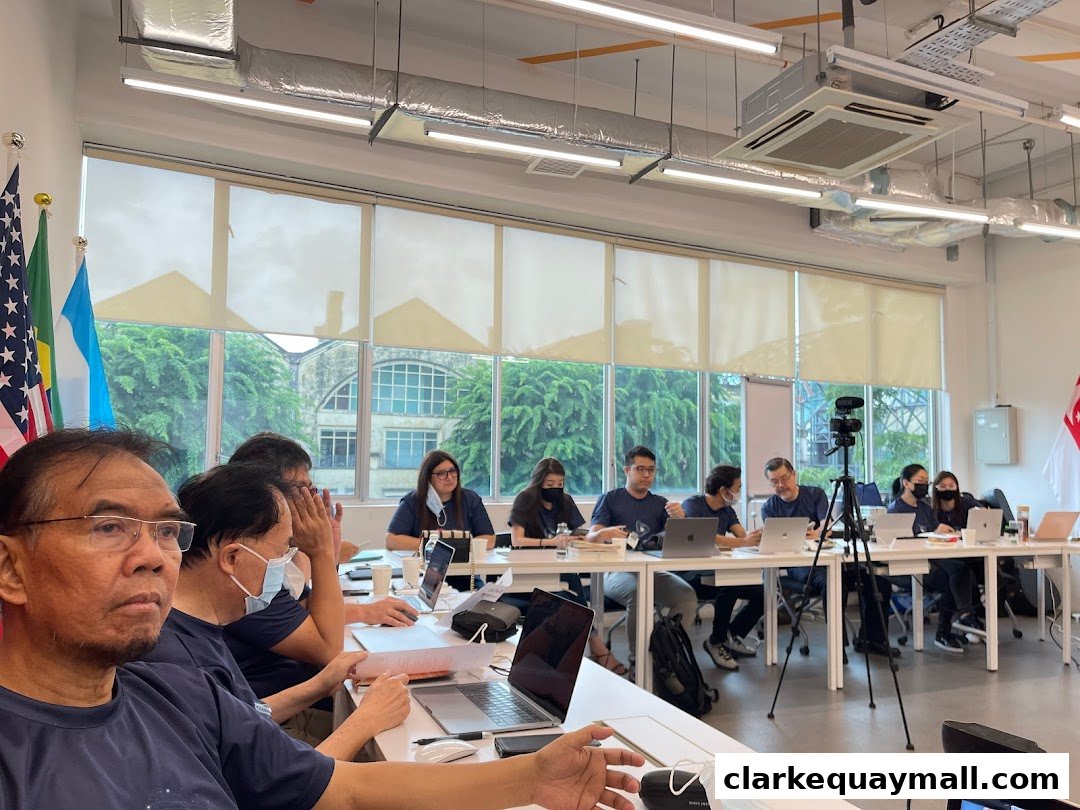 A group of people are seated at a long table in a modern office, engaged in a meeting.