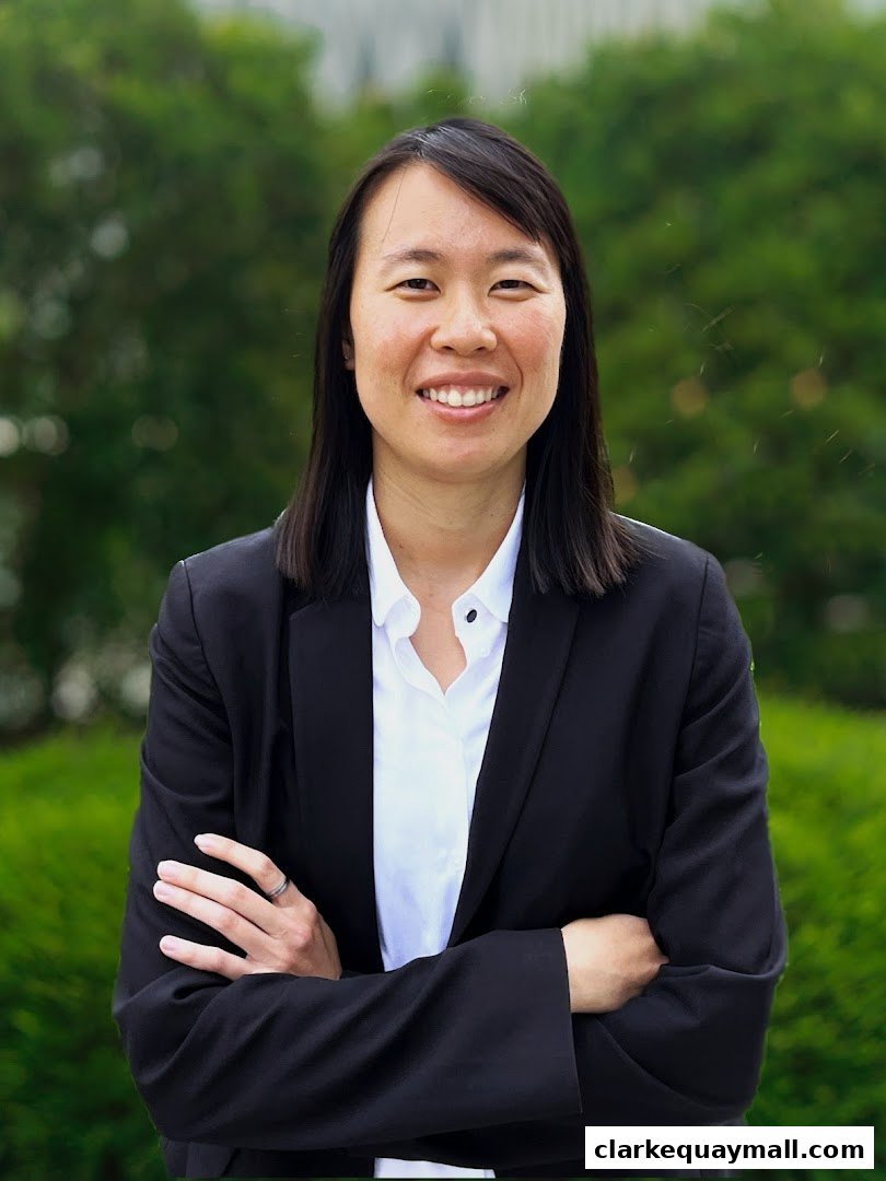 A professional portrait of an Asian woman in a black suit and white shirt, with arms crossed.