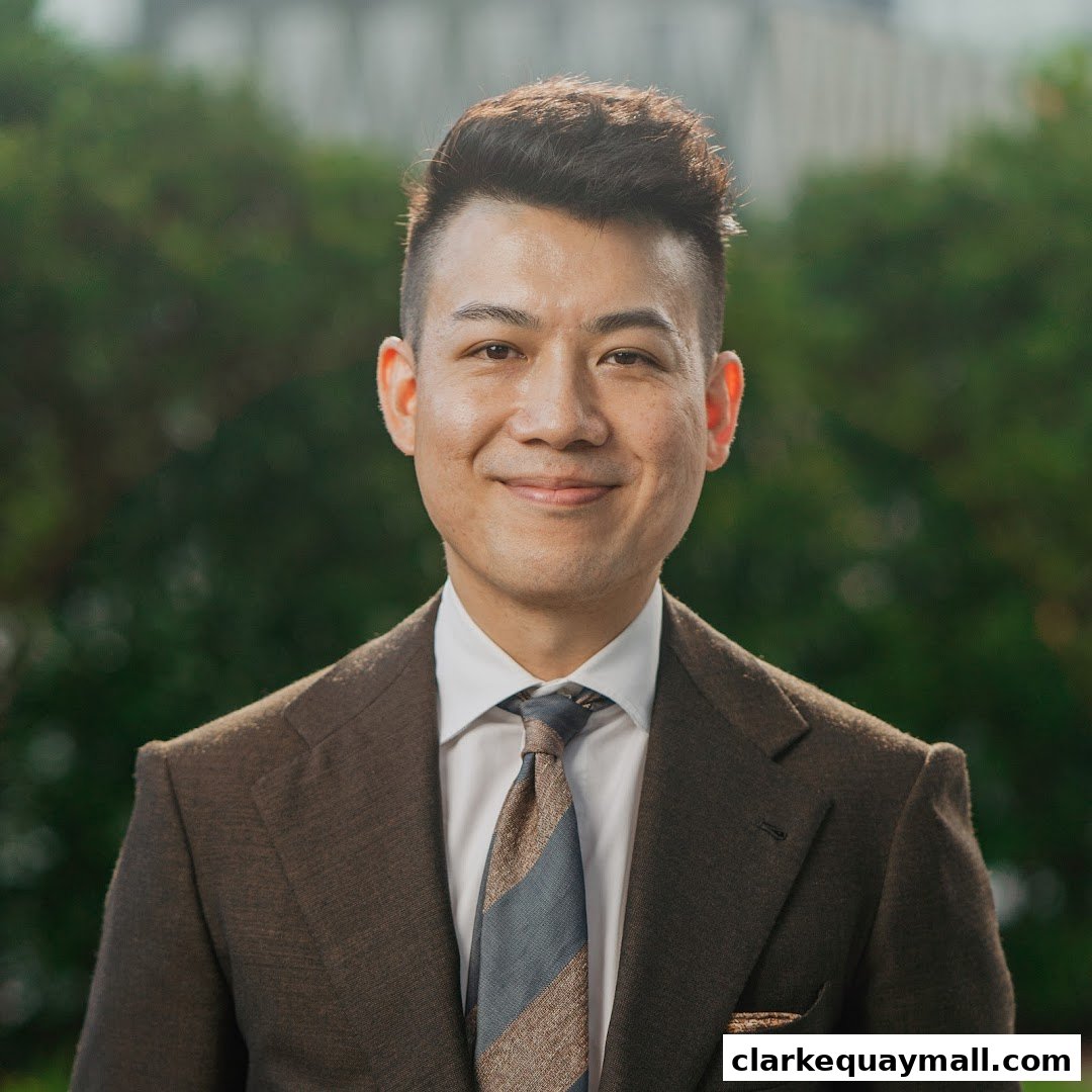A smiling man in a brown suit and tie stands in front of a blurred green background.