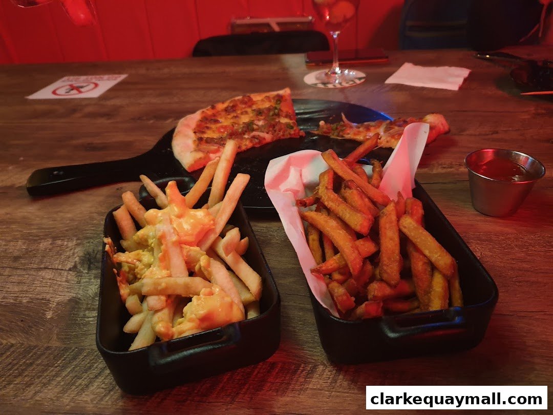A table at Coyote Ugly Saloon with pizza, cheese fries, regular fries, and a small cup of ketchup.