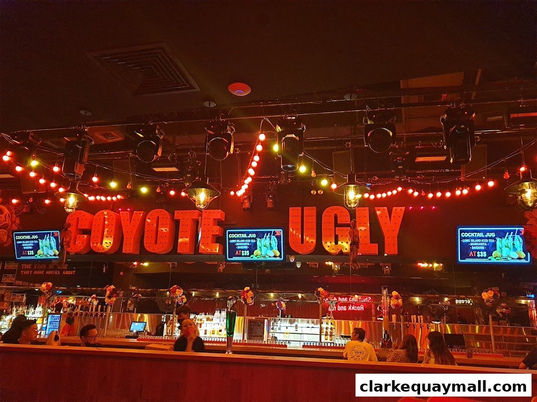 The interior of Coyote Ugly Saloon with a large illuminated sign and a bar with patrons.