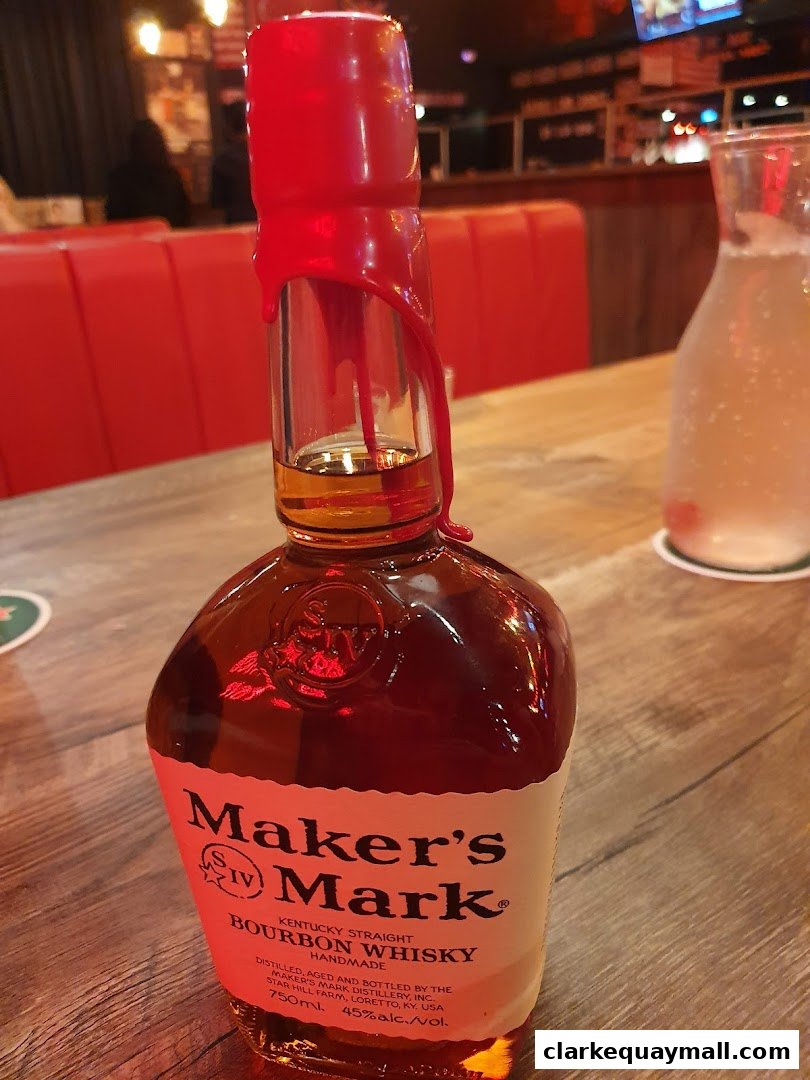 A bottle of Maker's Mark Bourbon Whisky sits on a wooden table in a dimly lit bar.