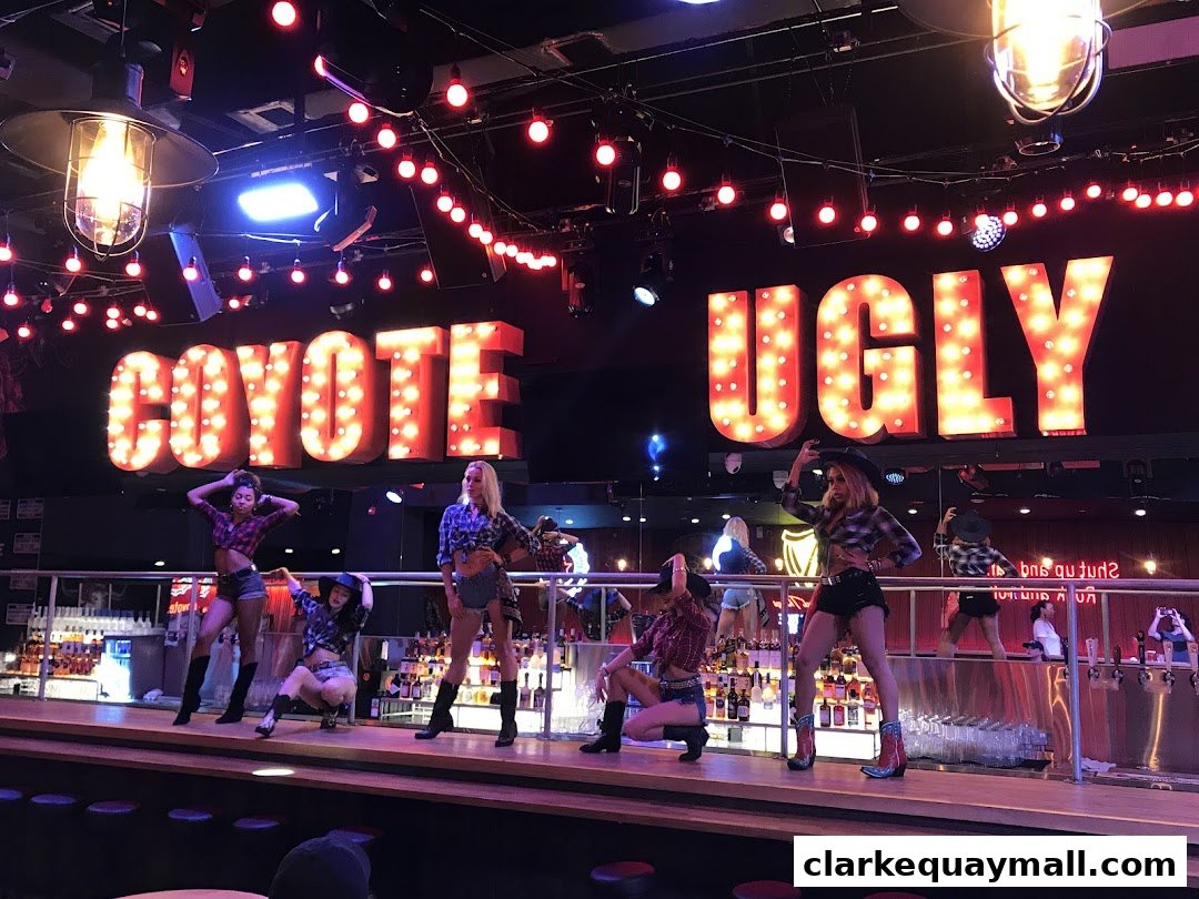 Dancers perform on stage at Coyote Ugly Saloon Singapore with illuminated signage.