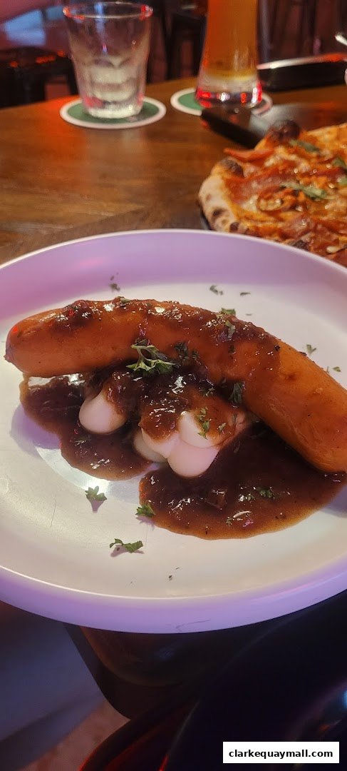 A plate of sausage and mashed potatoes with gravy, next to a pizza and drinks.