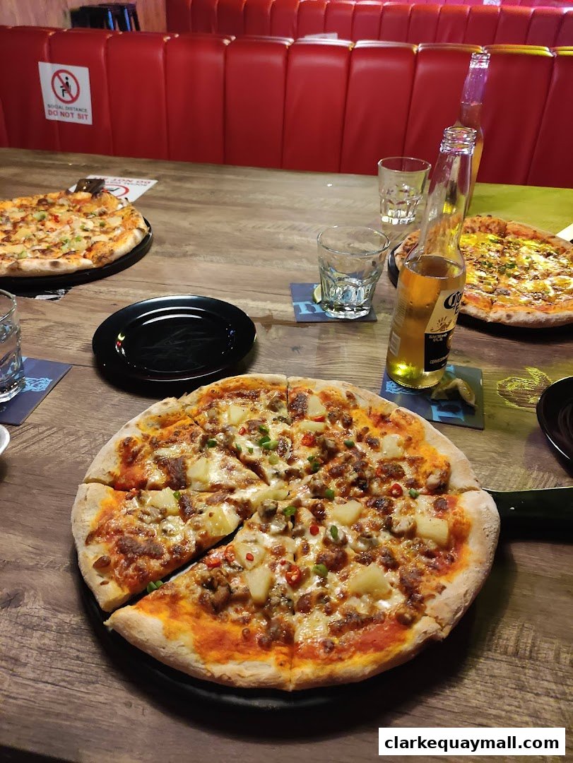 Pizzas and beers served on a wooden table with red booth seating in the background.