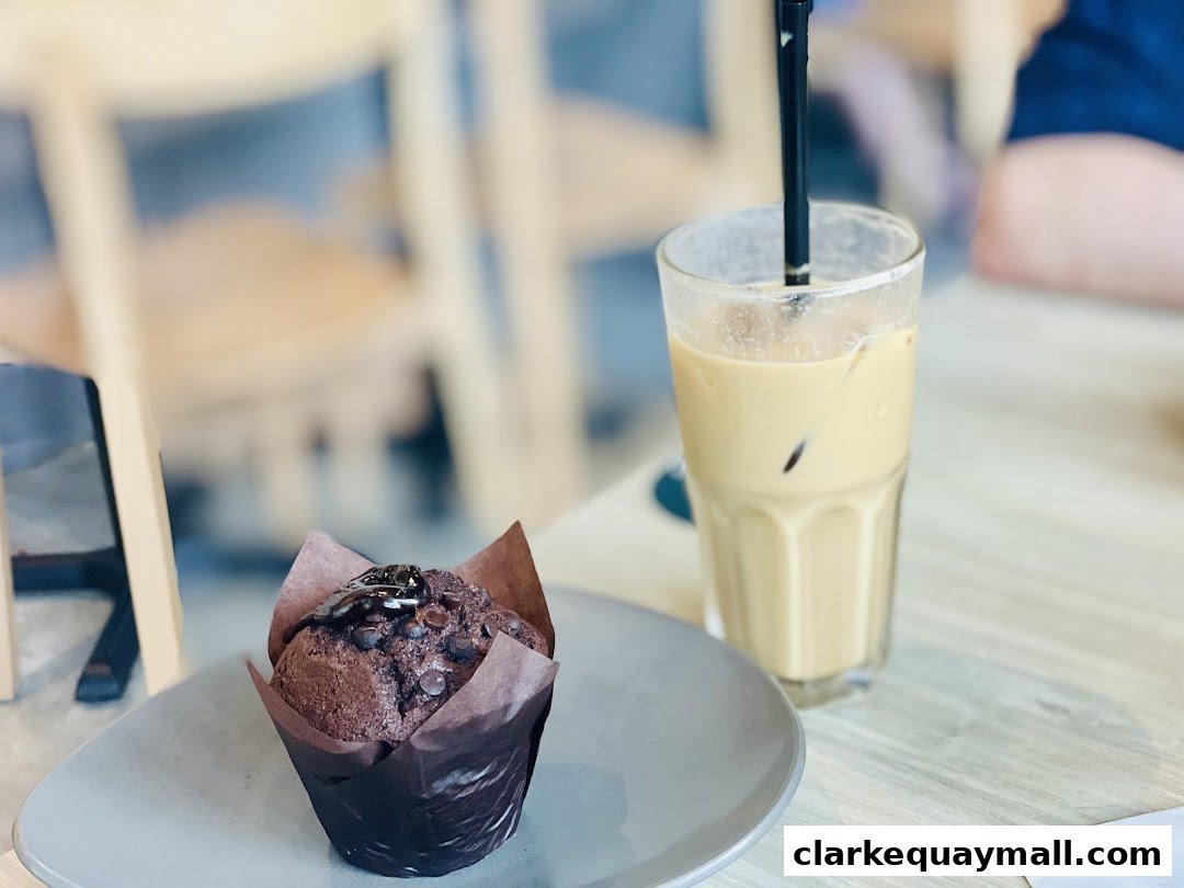 A chocolate muffin with chocolate chips and a glass of iced coffee on a table.