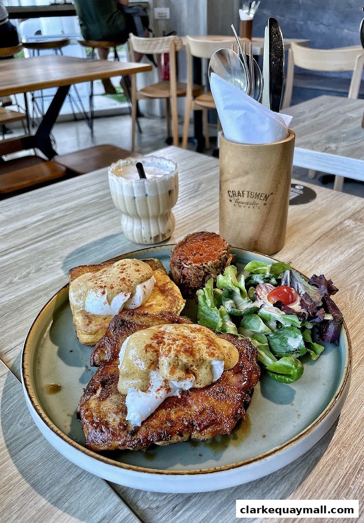A plate of chicken and eggs benedict with a side salad and a coffee drink.