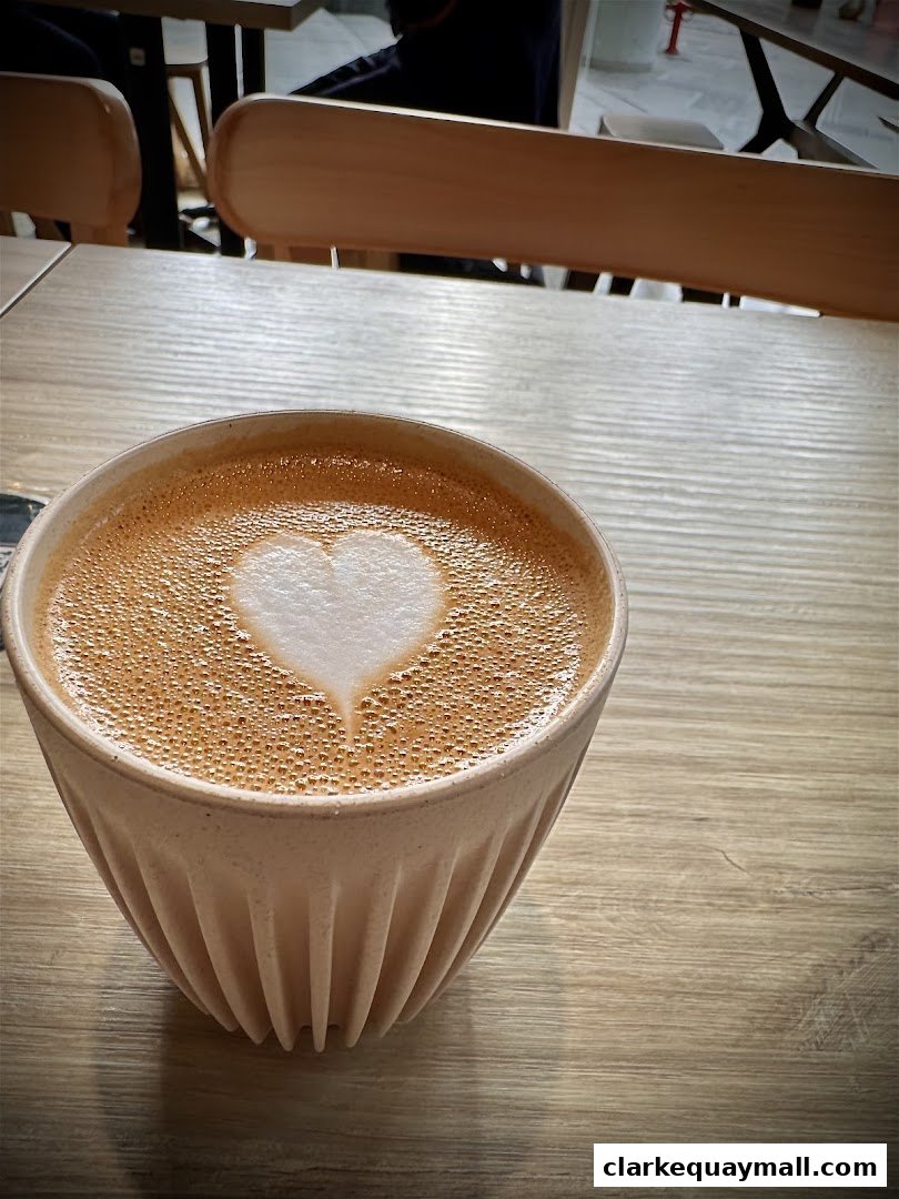 A close-up of a latte with heart-shaped latte art in a ribbed cup on a wooden table.