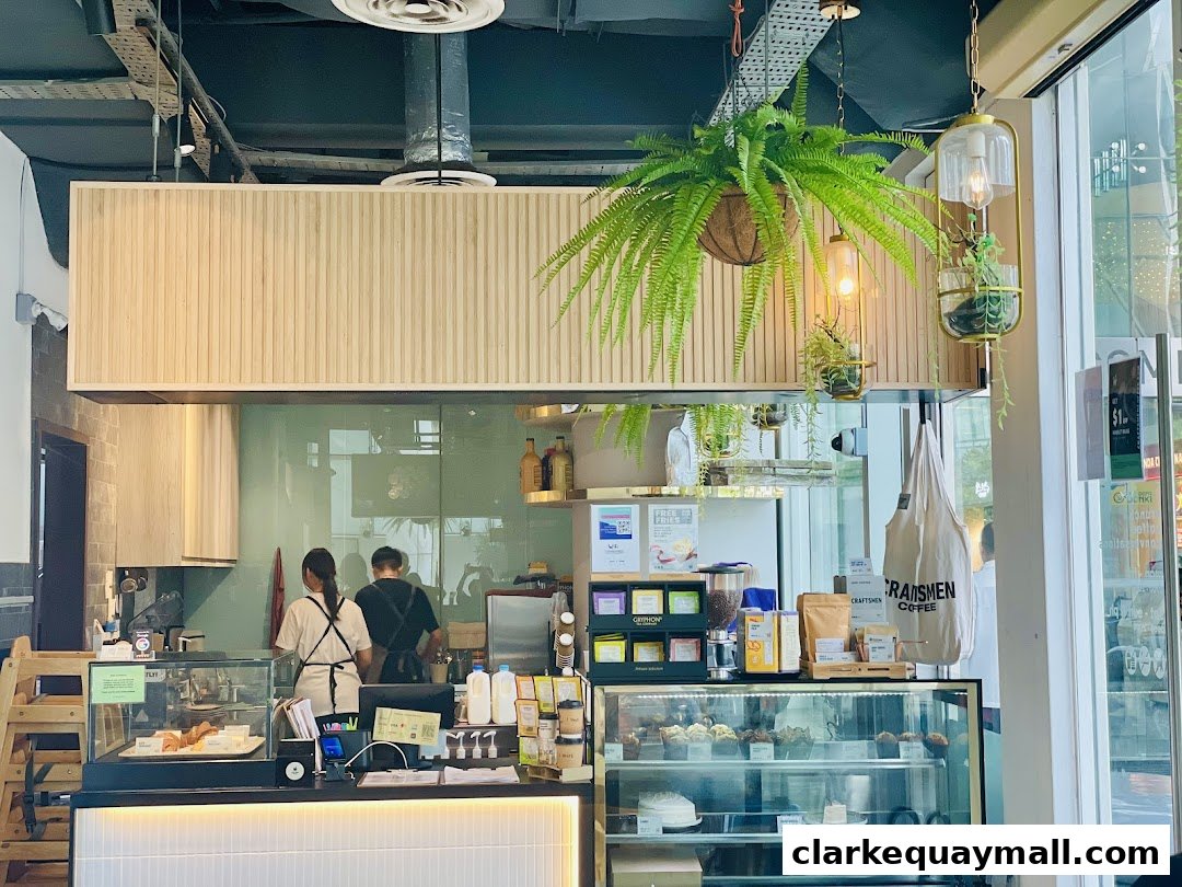 Interior view of Craftsmen Coffee with baristas, display cases, and hanging plants.