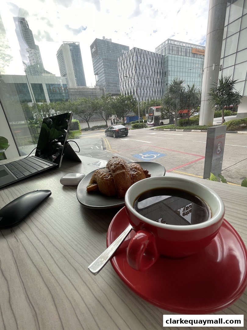 A cup of coffee and croissant on a table with a laptop and city view.