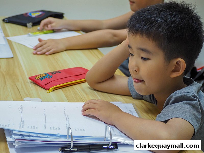 A young boy is focused on his studies at a desk with papers and a pencil case.
