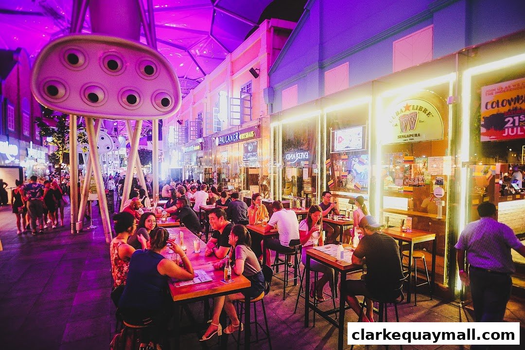 People dining and socializing at outdoor tables in front of a brightly lit bar at night.