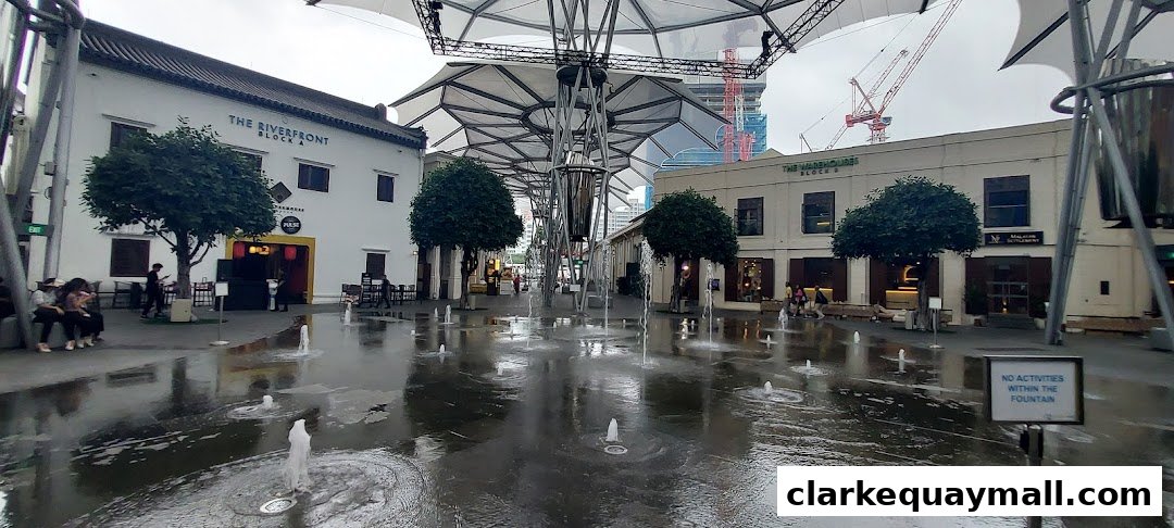 A public plaza with fountains and shops under a modern canopy.