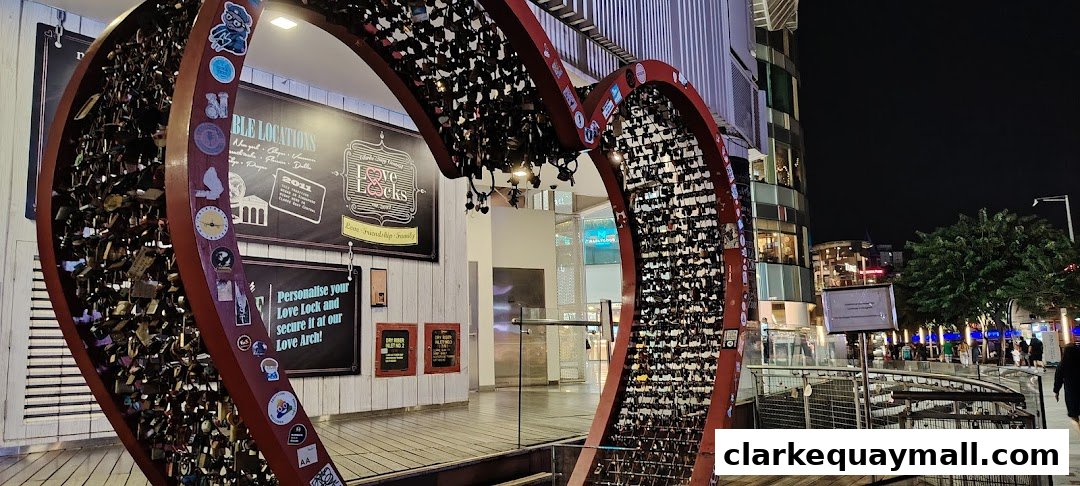 A large heart-shaped structure adorned with numerous locks, set against a backdrop of a shopping mall at night.