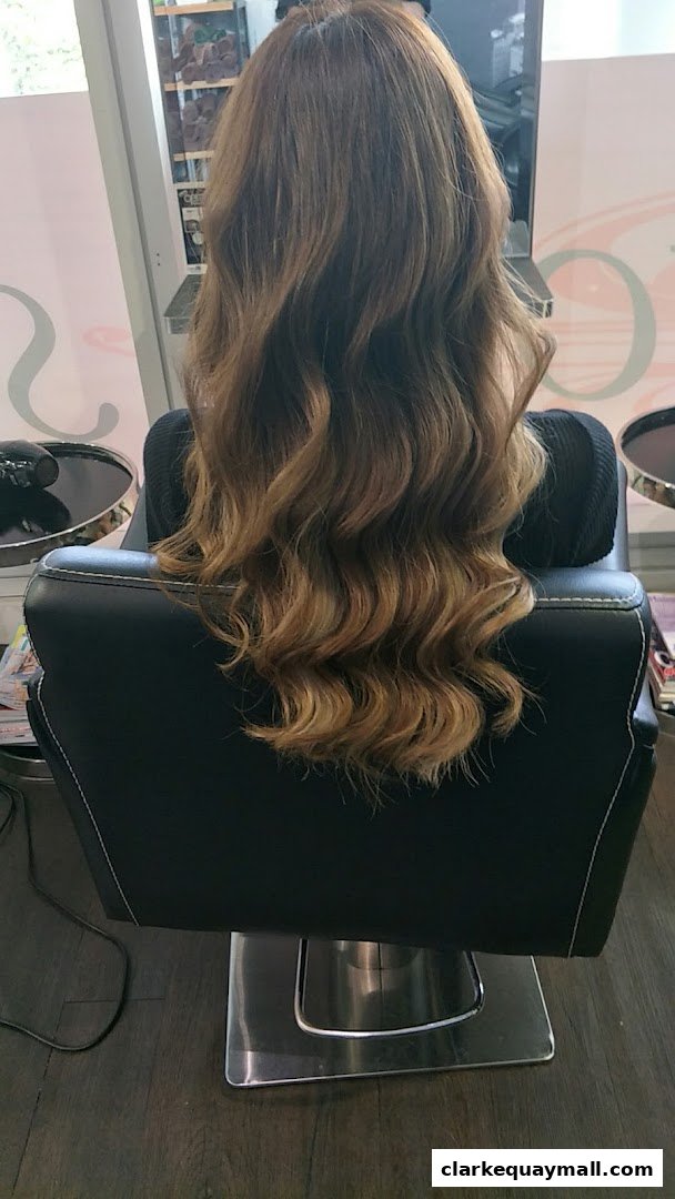 A person with long, wavy, brown hair sitting in a salon chair.