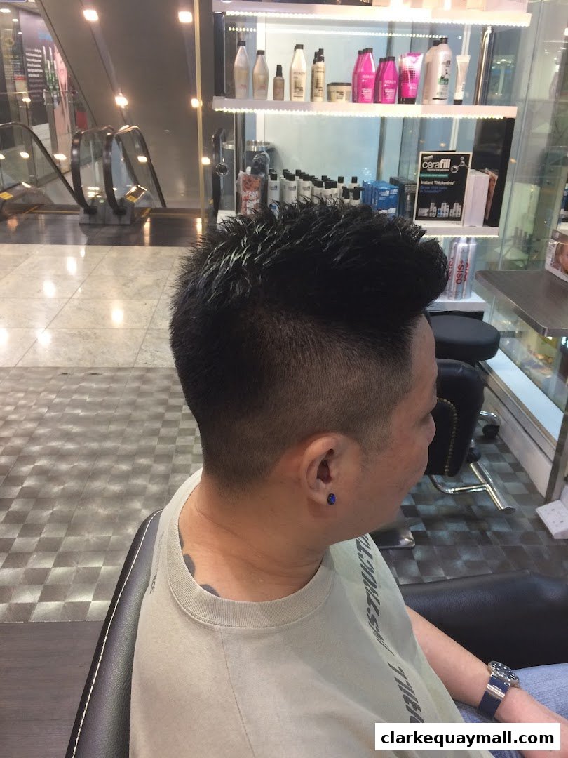 A person with a stylish haircut sits in a salon chair, with shelves of hair products in the background.