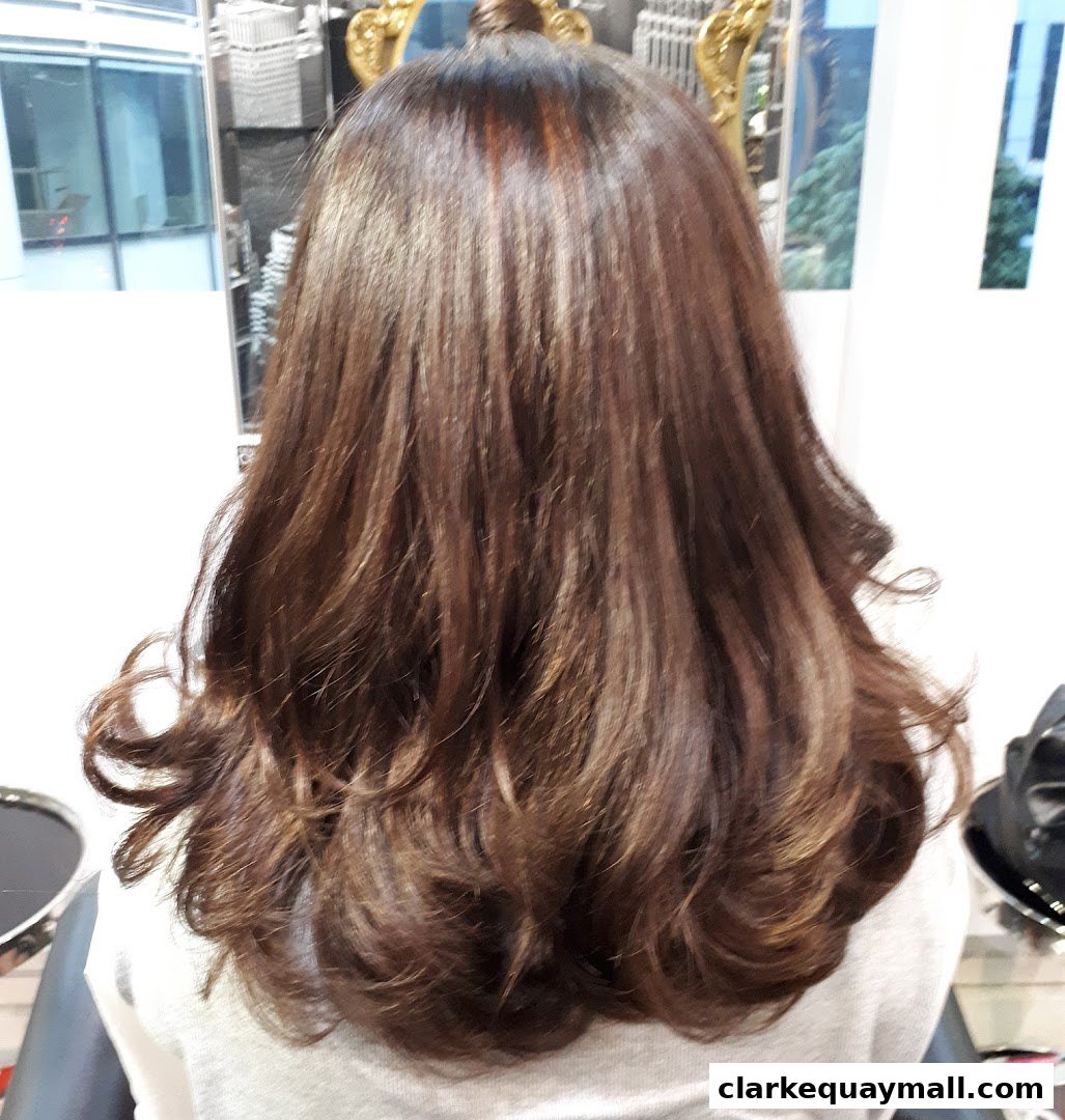 A person's back with beautifully styled, long, brown hair with highlights.