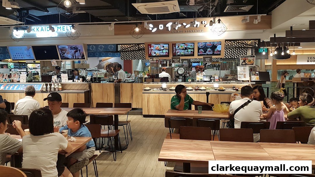 People dining at tables in a busy food court with various food stalls visible.