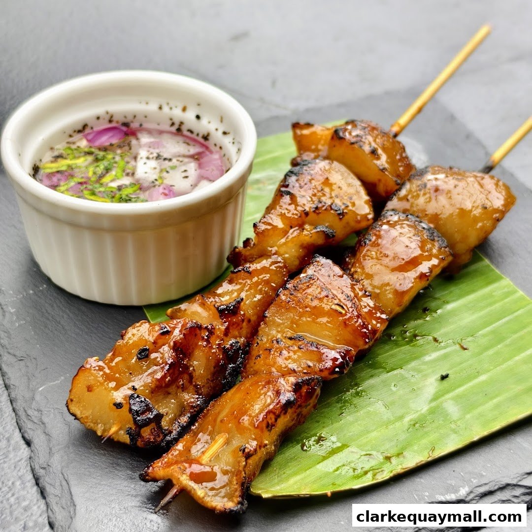 Close-up of grilled pork skewers with a dipping sauce on a banana leaf.