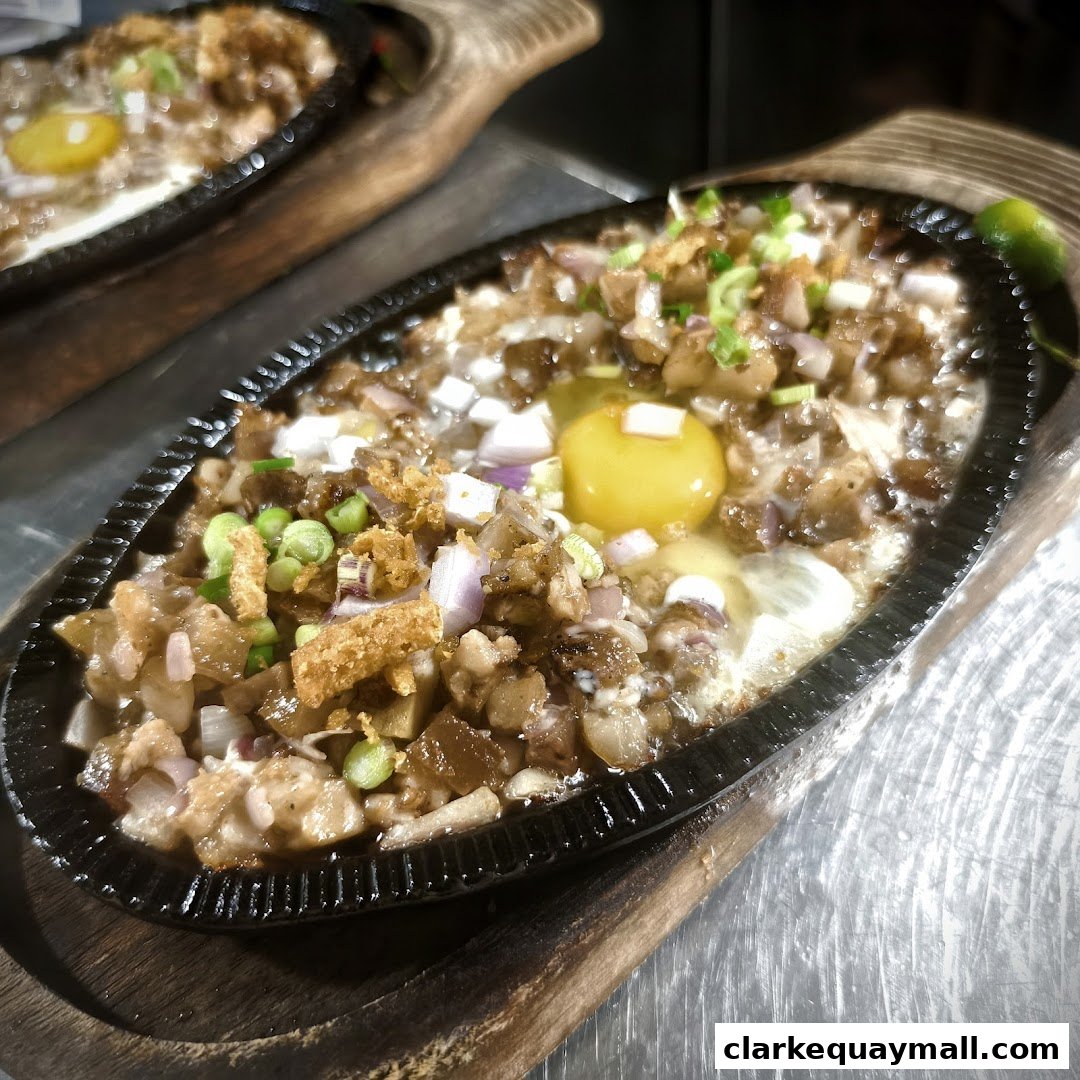 A sizzling plate of Filipino Sisig with a raw egg and chopped onions.
