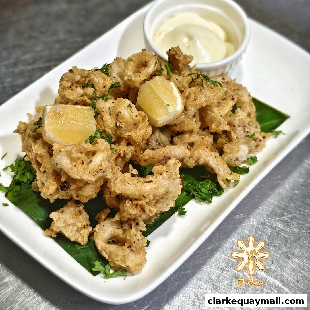 A plate of crispy fried calamari with lemon wedges and a side of dipping sauce.