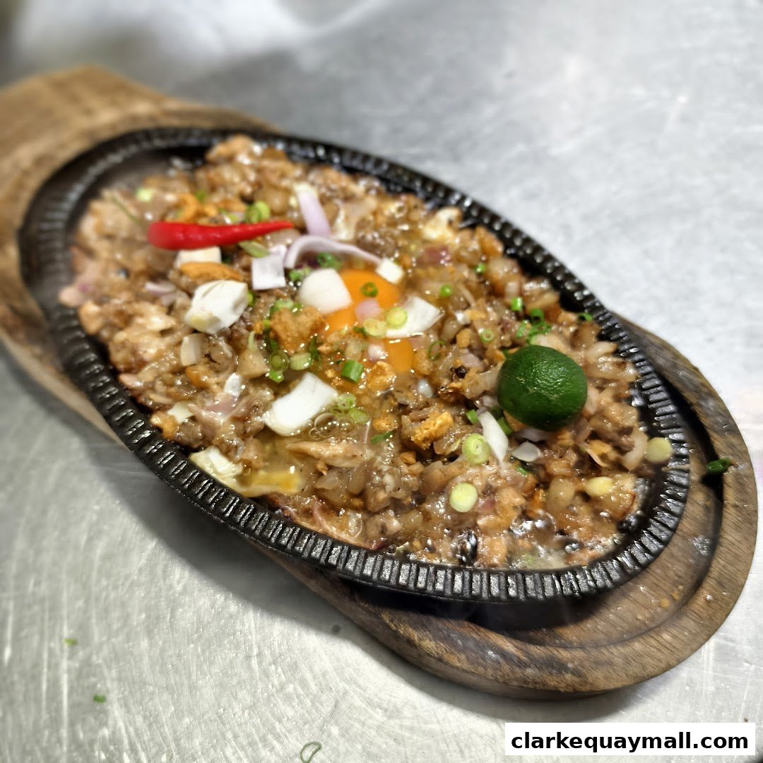 A sizzling plate of Filipino Sisig, a popular dish, served with a raw egg and lime.