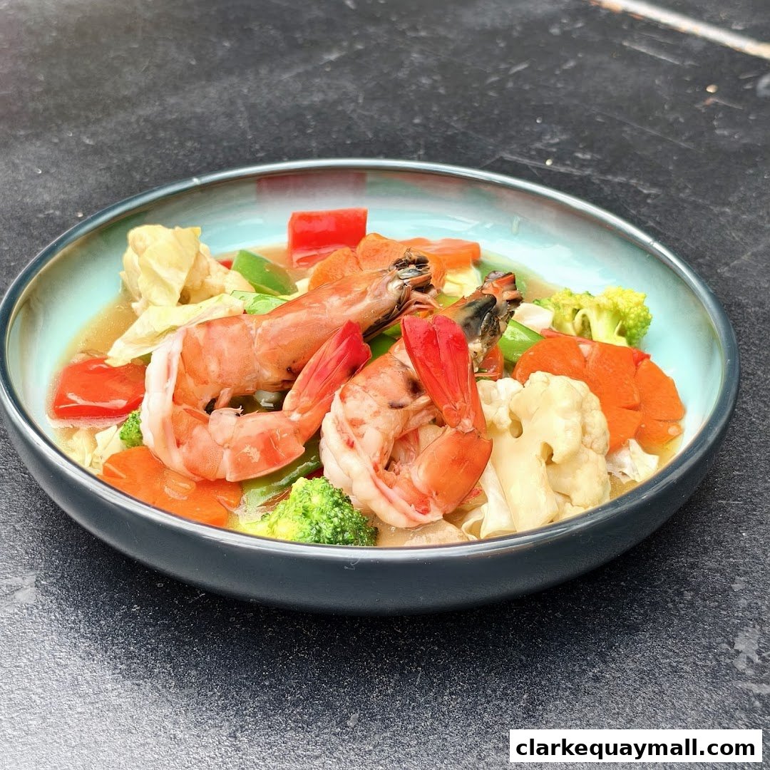 A close-up of a seafood dish with large prawns and mixed vegetables in a light sauce.