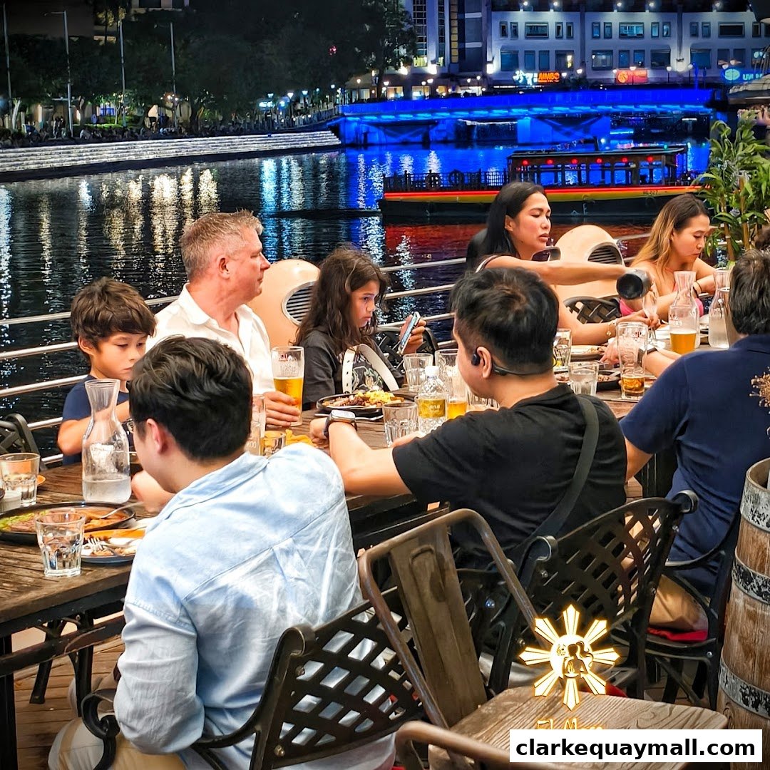 A group of people enjoying a meal at El Mesa Filipino Seafood Grill by the river at night.