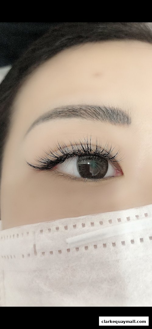 Close-up of a woman's eye with dramatic false eyelashes and a medical mask.