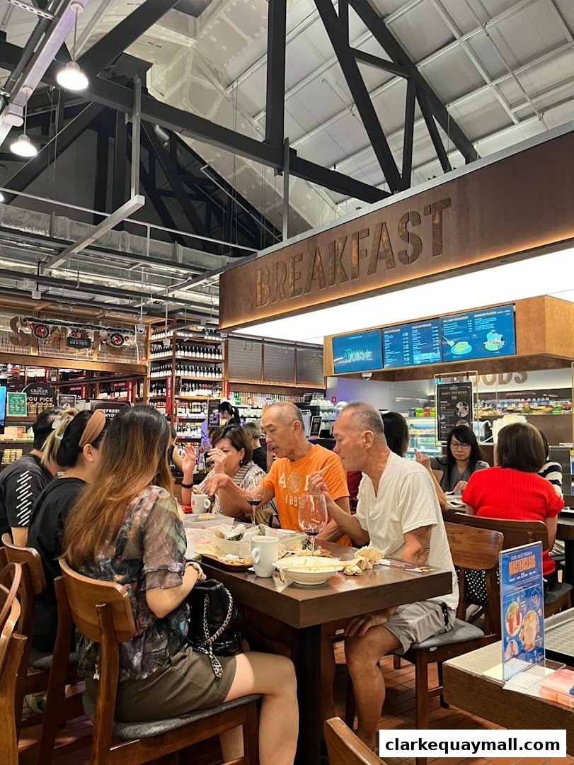 People dining at tables inside a FairPrice Finest supermarket with a 'BREAKFAST' sign overhead.
