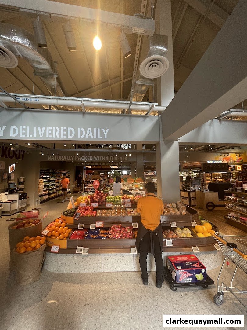 A grocery store employee arranges fruit on display shelves, with various produce and shopping carts visible.