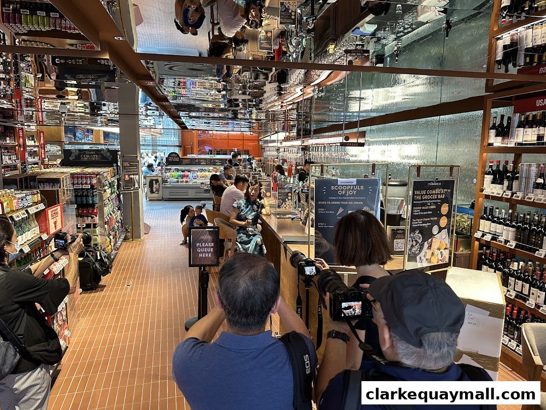 People are filming and taking photos inside a well-stocked grocery store with a bar area.