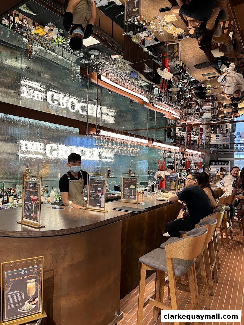 A bartender serves customers at a stylish bar with mirrored ceilings and hanging wine glasses.
