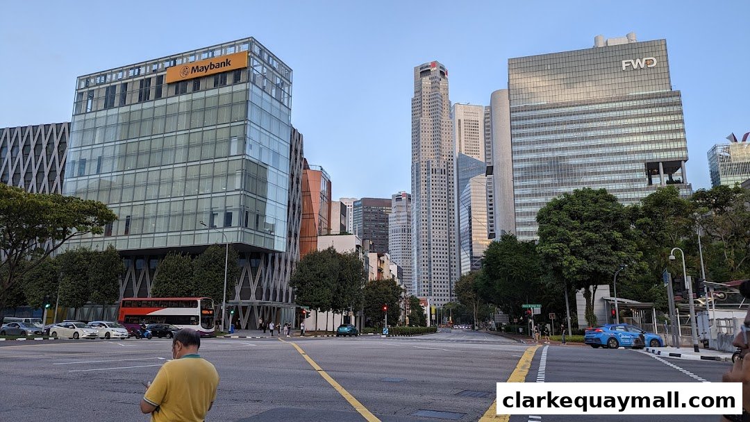 A street view of modern city buildings, including Maybank and FWD, with traffic and pedestrians.