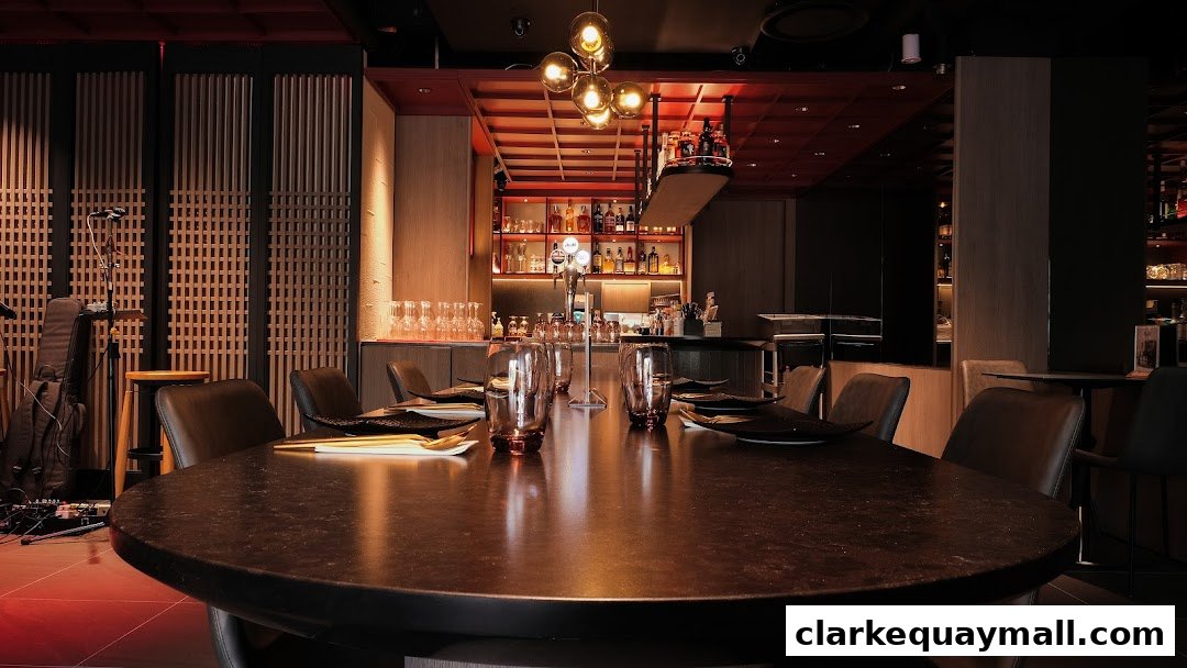 A dimly lit restaurant interior with a large round table set for dining and a bar in the background.
